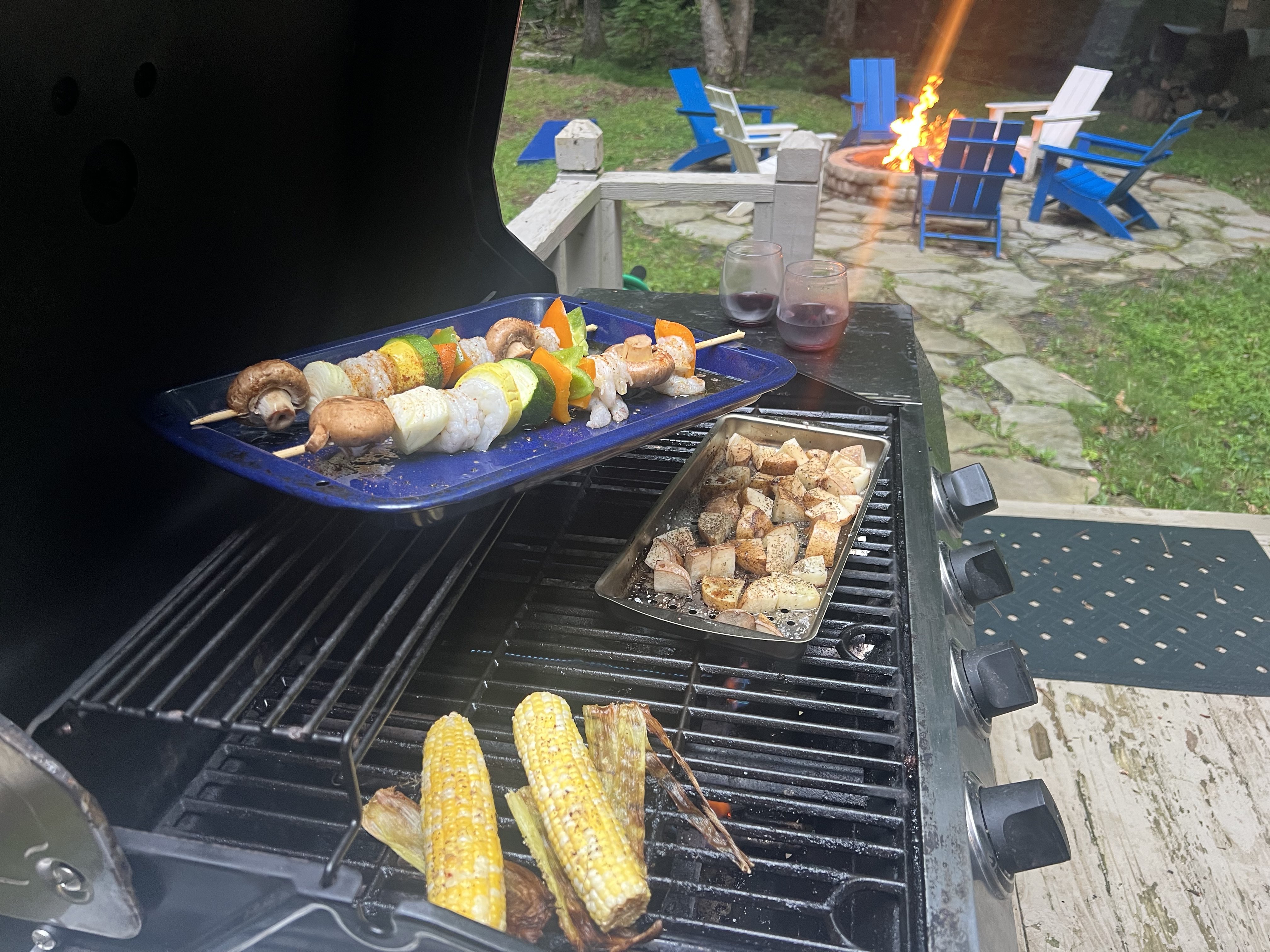 Kebabs, corn, and chicken on the grill at Fish Head Lodge with the firepit and blue Adirondack chairs in the background